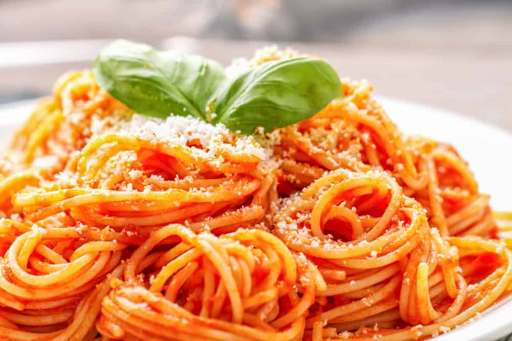Spaghettiret med parmesan og basilikum blade på toppen.